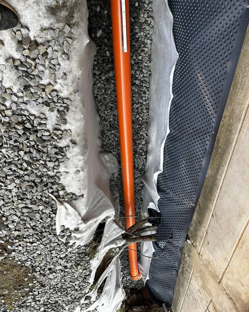 Drenážna rúra v štrkovom lôžku s geotextíliou a nopovou fóliou pri stene domu